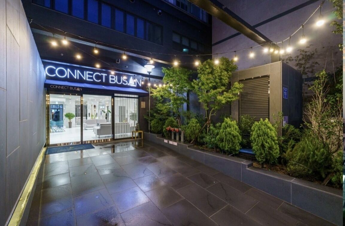 Un edificio moderno con un letrero que dice 'CONNECT BUSAN', zona de estar al aire libre y un jardín bien cuidado.