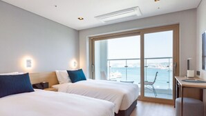 A modern hotel room with two beds, a desk, and a large sliding glass door leading to a balcony with a city view. - Busan Connect Ocean Hotel (Busan)