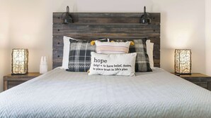 Un lit bien fait, avec une tête de lit à motifs chevrons, deux lampes de chevet et un coussin aux motifs inspirants.