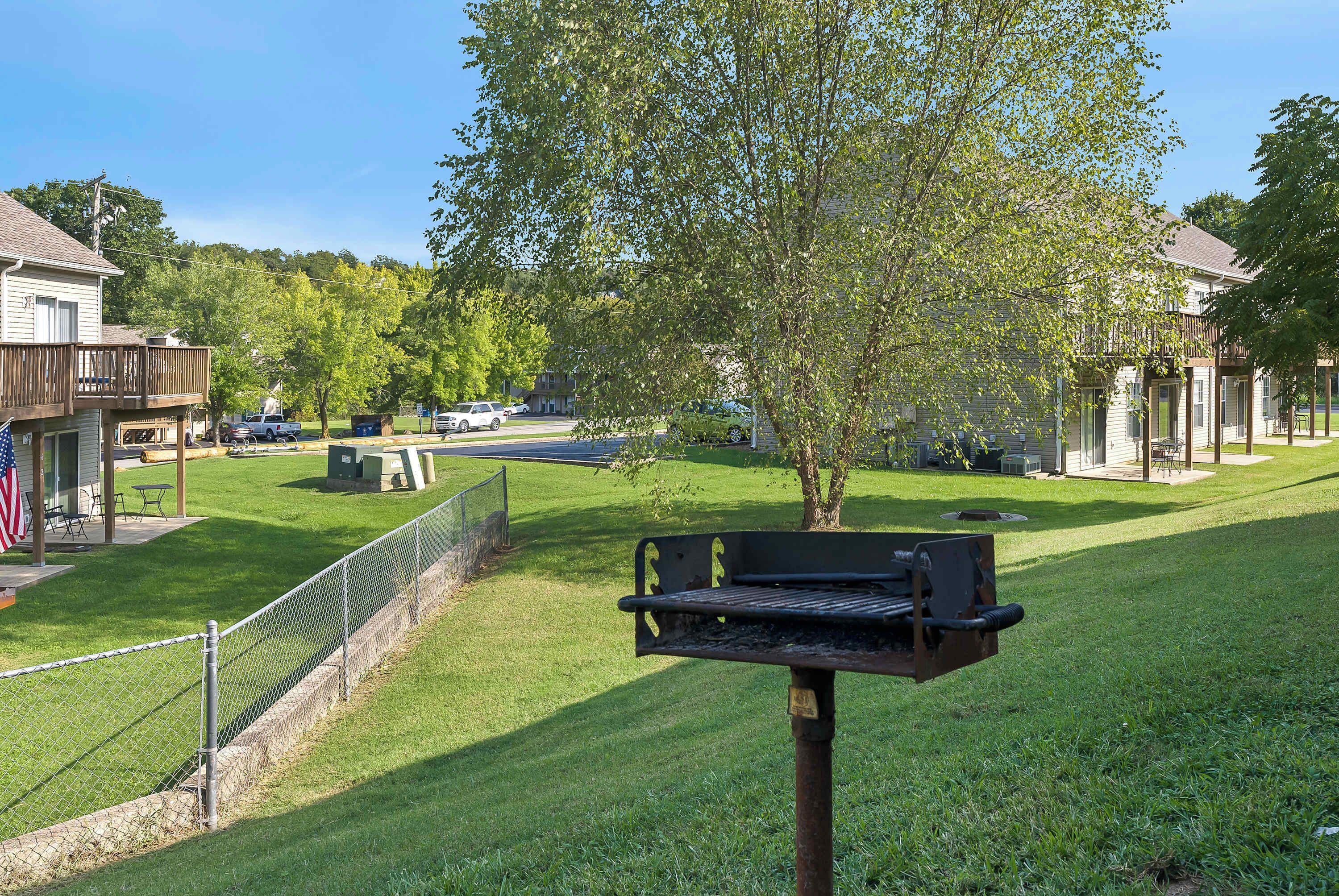 A backyard with a grill, a fenced area, and a tree.
