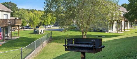 A backyard with a grill, a fenced area, and a tree.