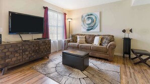 Un salon avec un téléviseur, un canapé, une table basse et un tapis.