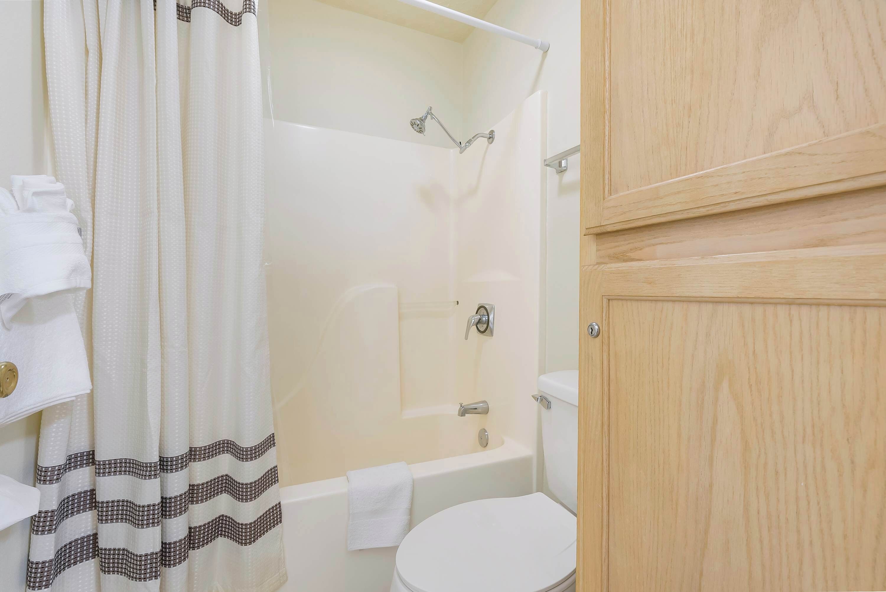 A bathroom with a shower, toilet, and wooden cabinet.