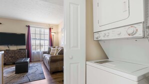 Une buanderie équipée d’un lave-linge et d’un sèche-linge à chargement frontal, d’un téléviseur à écran plat fixé au mur, d’un canapé et d’un pouf à motifs imitant des briques.