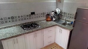 Une cuisine avec des armoires blanches, une cuisinière à gaz, un évier et un réfrigérateur.