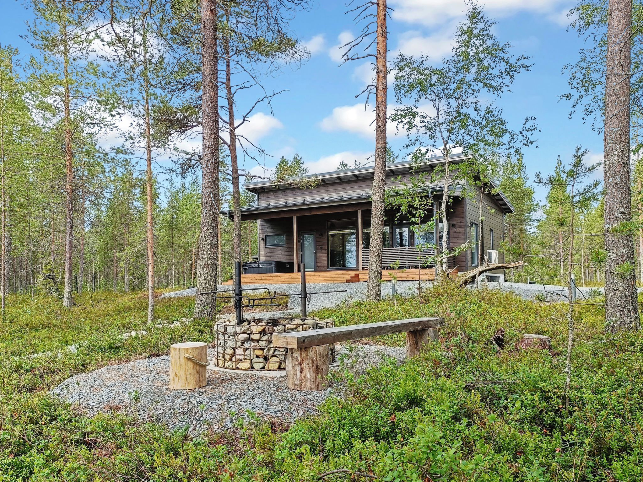 Une cabane dotée d’une cheminée en pierre, d’une terrasse en bois et entourée d’une forêt.