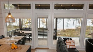 Ein modernes Interieur mit einem Holzesstisch, einer schwarzen Ledersofa und Blick ins Freie durch große Glastüren.