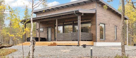 Eine moderne Holzjagdhaushütte mit überdachter Veranda, großen Fenstern und einem Schotterweg.