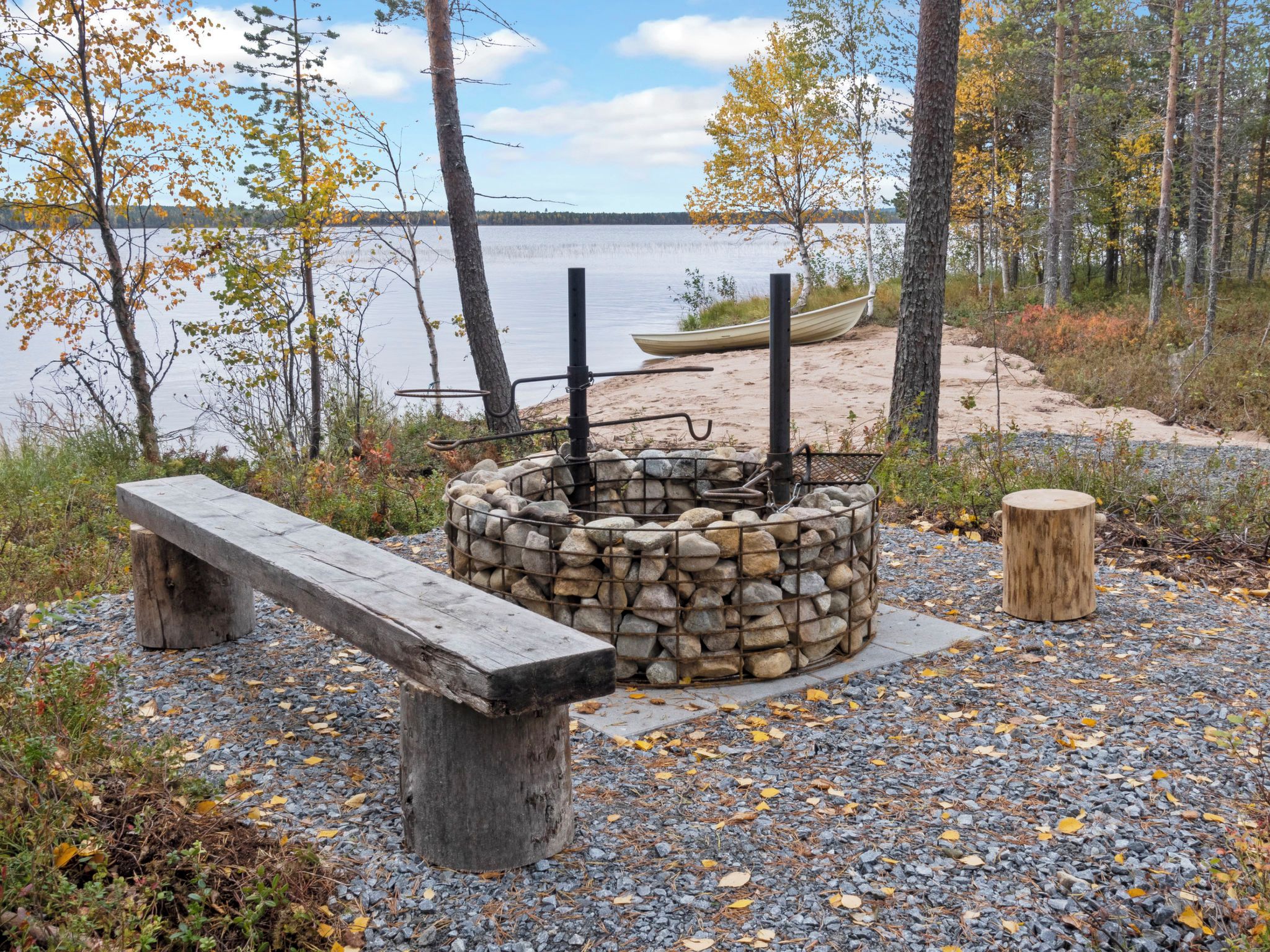 En campingplats vid sjön med en eldstad av sten, en träbänk och en kanot.