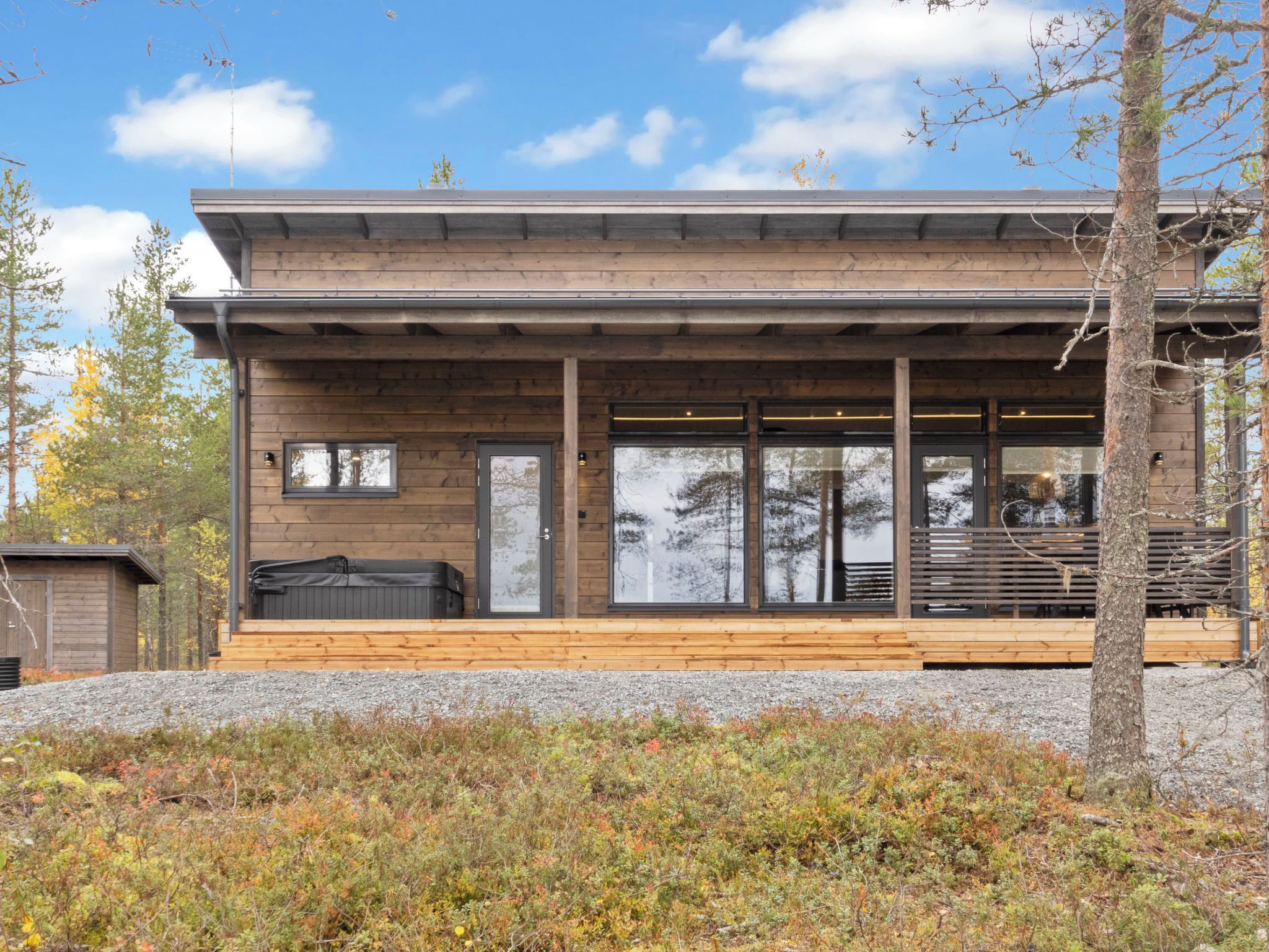 A modern wooden cabin with a covered porch, large windows, and a grill outside.