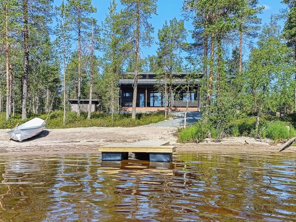 Una cabaña con un muelle que se adentra en un lago, rodeada de un bosque frondoso.