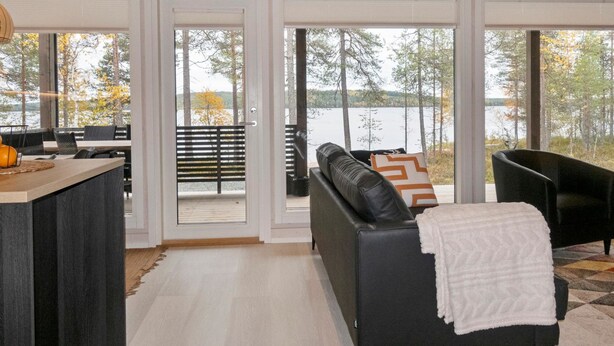 Ein modernes Wohnzimmer mit großem Fenster mit Seeblick, einem schwarzen Ledersofa und einem Holztisch.
