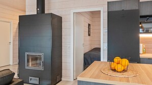 Ein modernes Interieur mit Kaminofen, einem Essbereich mit Holztisch und einem gemütlichen Schlafzimmer mit Bett sowie einer Tür zu einem weiteren Raum.
