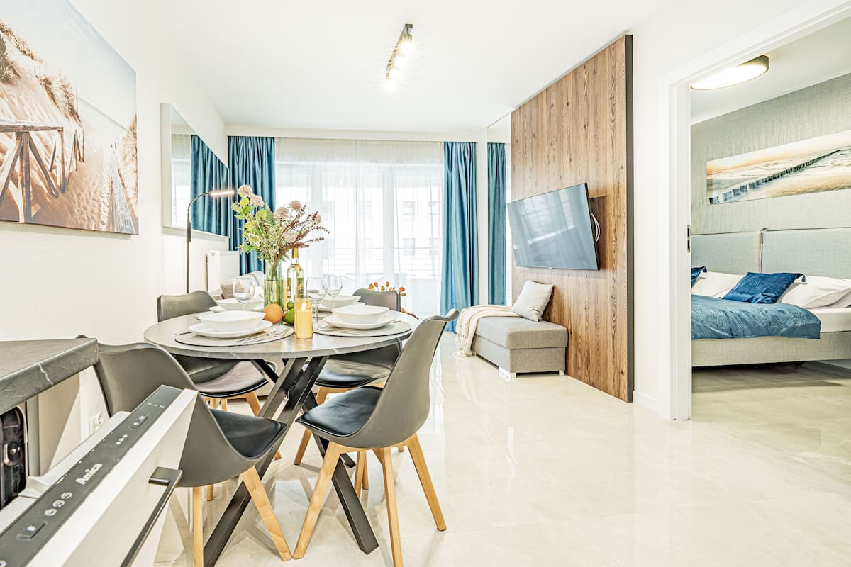 Een moderne woonkamer met een eethoek, een flatscreen televisie aan de muur en een bank met uitzicht op het strand.
