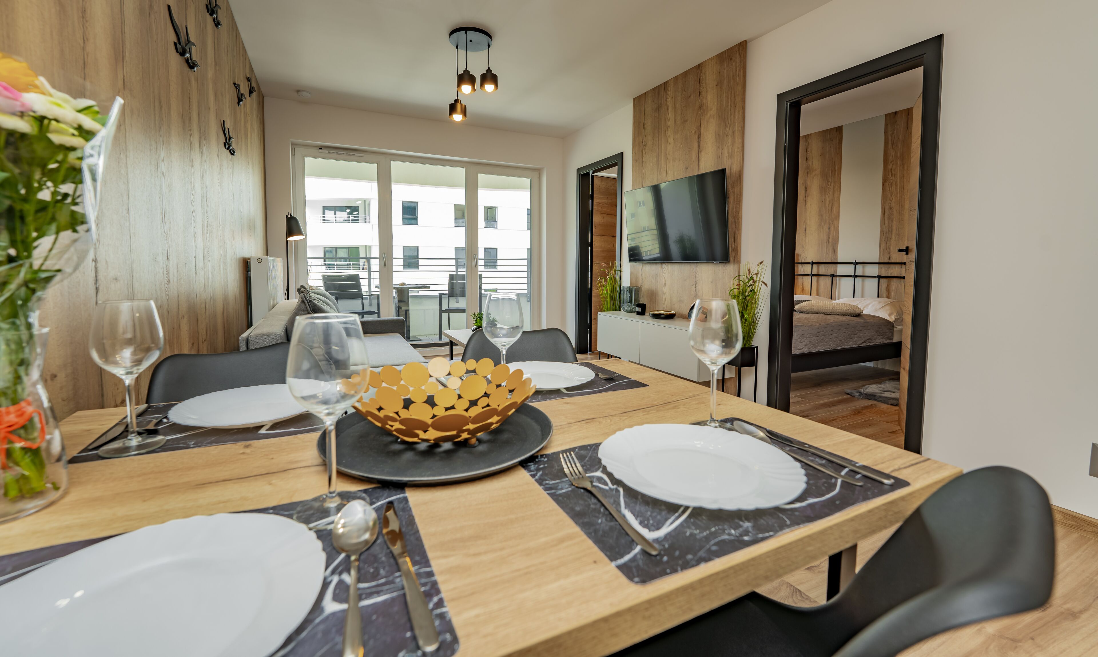 A dining area with a wooden table set for four, a large bowl centerpiece, and a TV mounted on the wall.