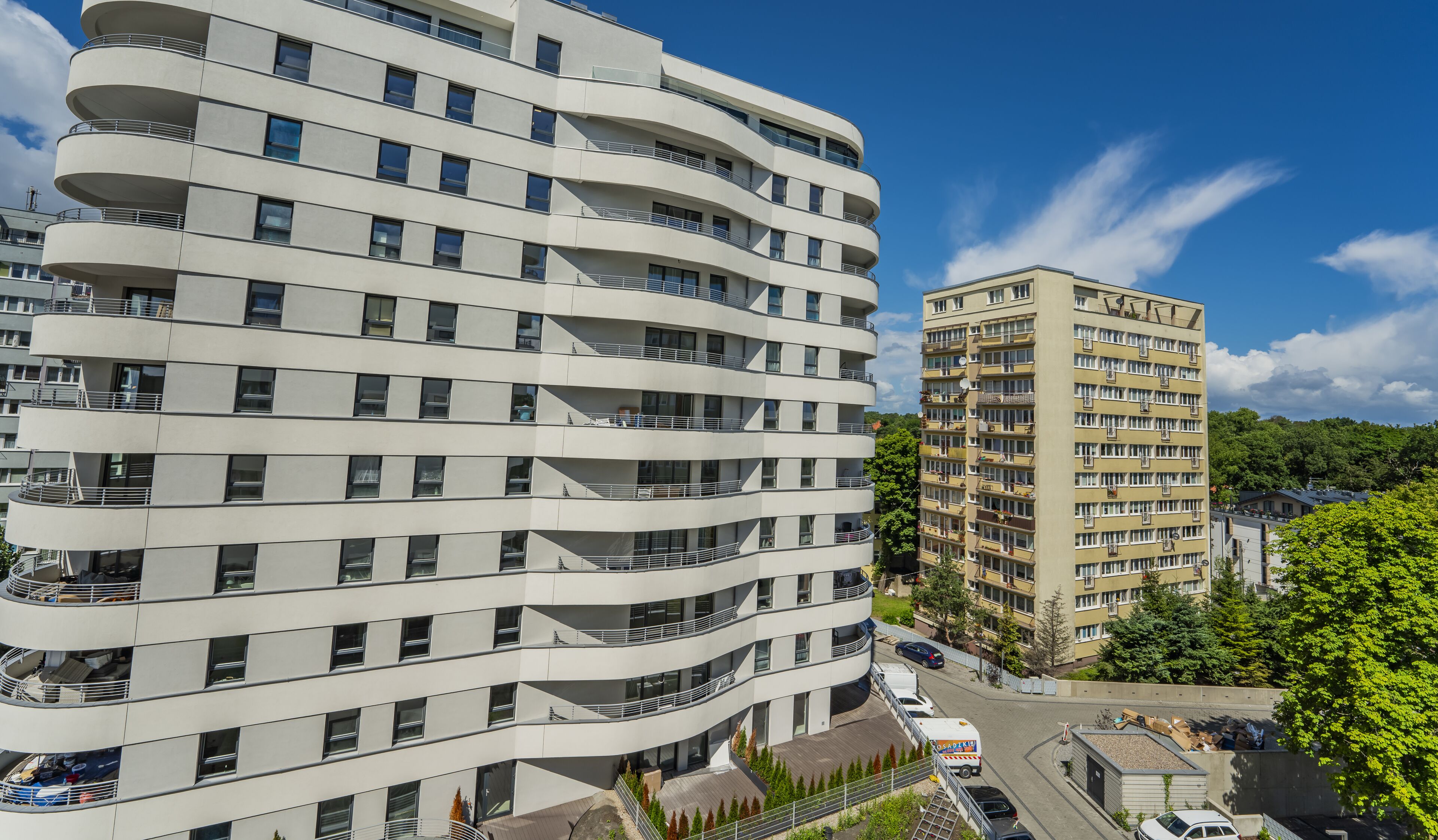 A multi-story building with balconies, a parking area, and a smaller adjacent building.