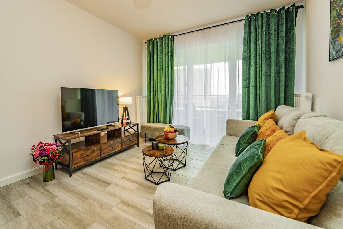 Een moderne woonkamer met een flatscreen televisie, een houten salontafel en een bank met kussens.