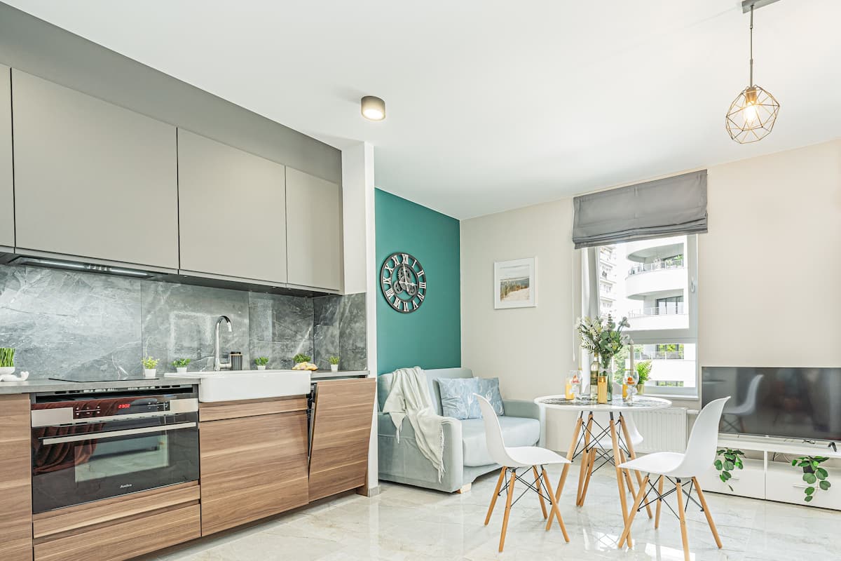 Een moderne keuken met inbouwapparatuur, een eethoek met een ronde tafel en stoelen, en een zithoek met een televisie en grote ramen.