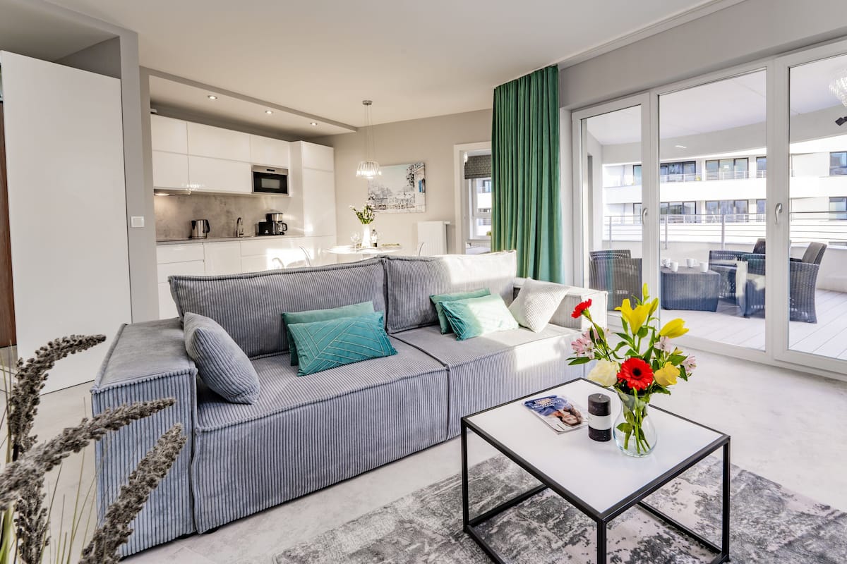 Een moderne woonkamer met een grijs gestreepte bank, een glazen salontafel en uitzicht op het balkon.