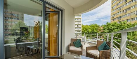A balcony with wicker furniture, a glass table, and a view of a building and trees.