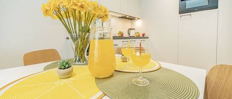 Una mesa de comedor con individuales amarillos, un jarrón con flores amarillas y una jarra de bebida amarilla.
