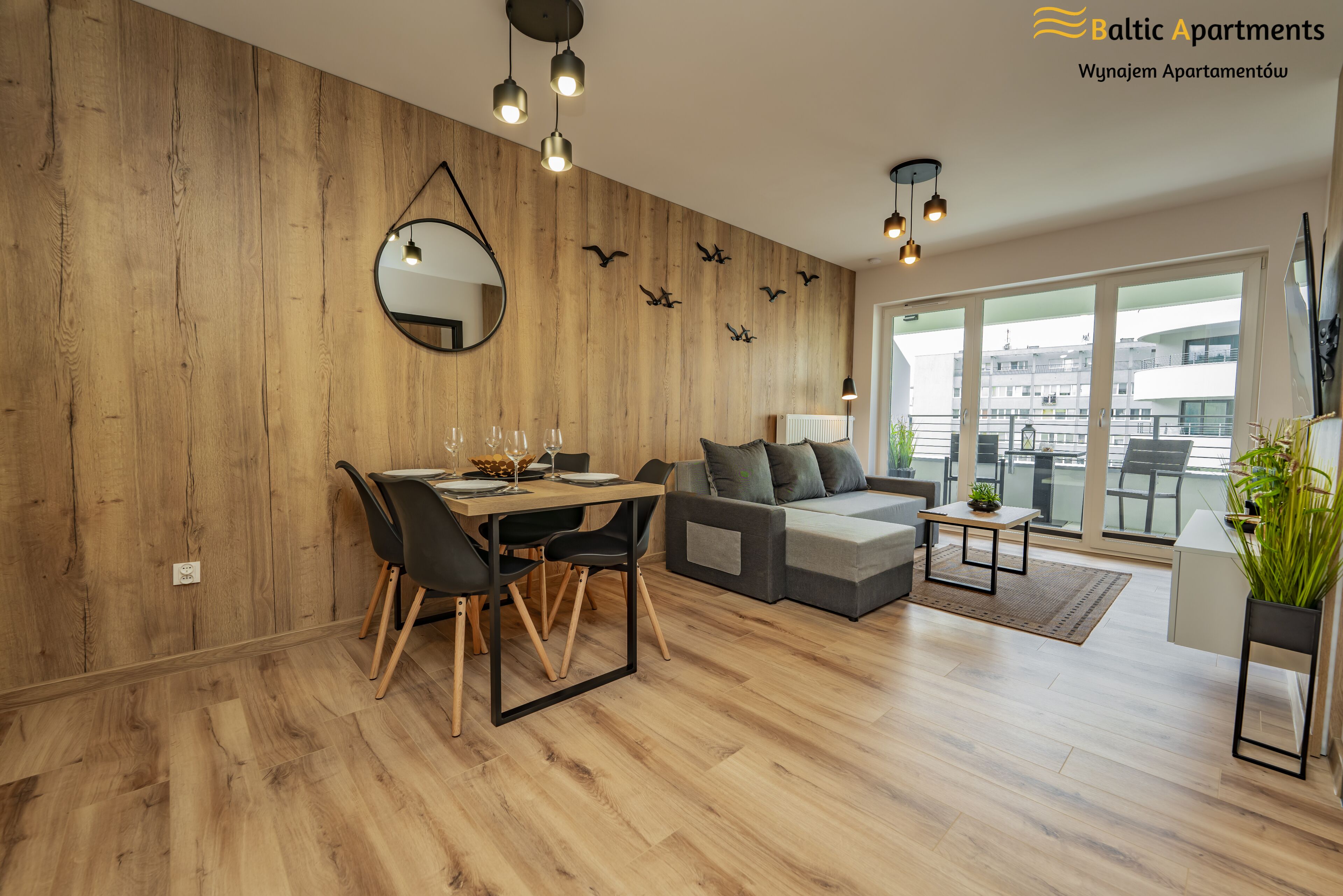 Una sala moderna con una pared de madera, un área de comedor con mesa y sillas, un sofá gris y un balcón con vistas.