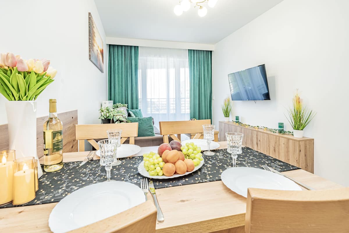 Een eetgedeelte met een tafel voor vier personen, een fles wijn, kaarsen en een fruitschaal.