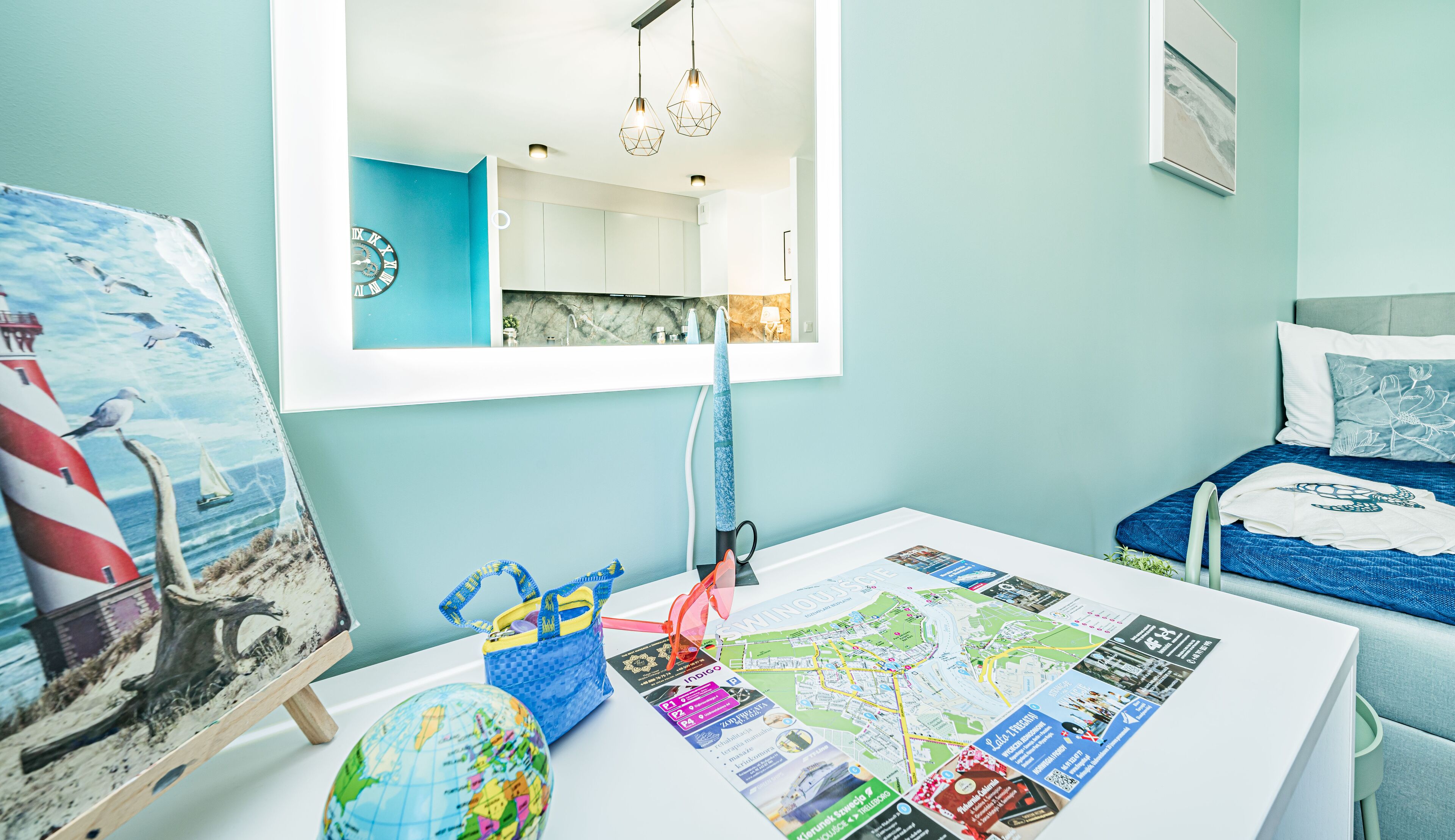 A child's room with a bed, a desk with travel maps and a globe, a mirror, and a painting of a lighthouse.