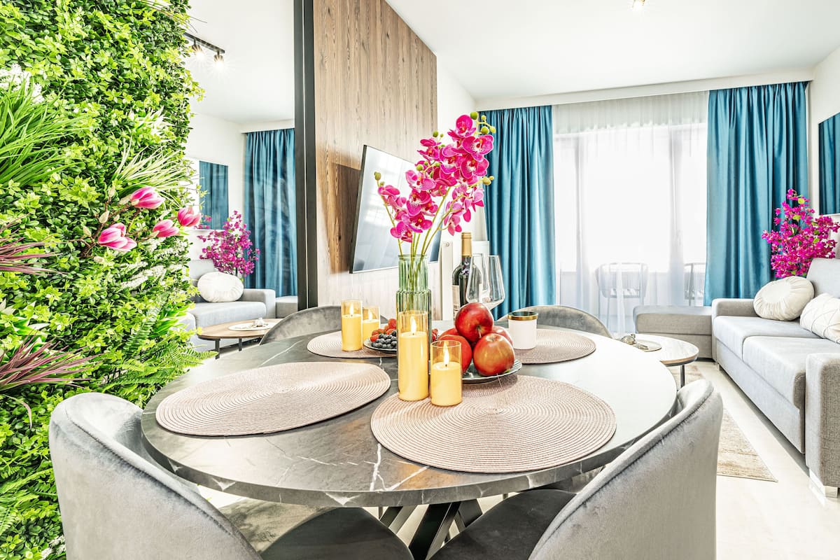 Een moderne woonkamer met een ronde eettafel, een grijze bank en een groot raam met blauwe gordijnen.