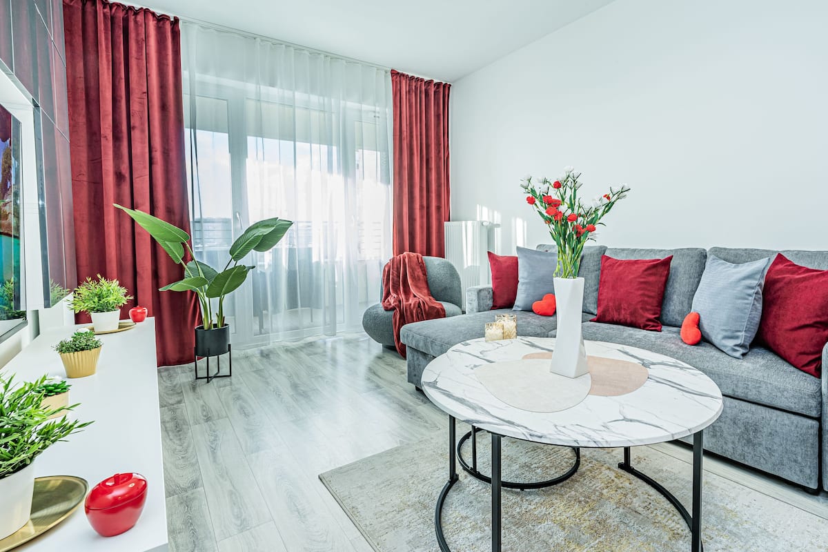 Een moderne woonkamer met een grijze bank, rode kussens, een witte vaas met bloemen en een marmeren salontafel.