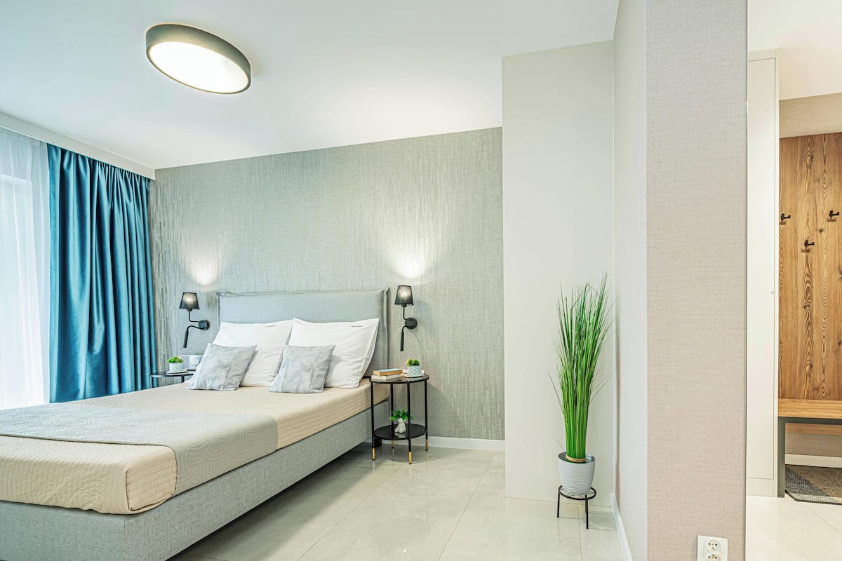 Een moderne slaapkamer met een bed, nachtlampjes, een klein tafeltje met een plant en een houten garderobe.