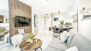 Een moderne woonkamer met een grijze bank, een houten salontafel en een eethoek met een tafel gedekt voor vier personen.