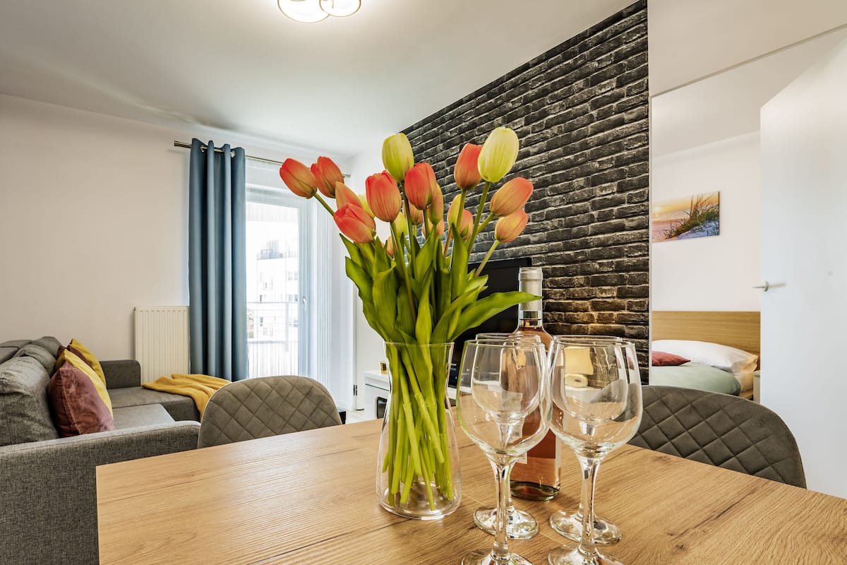 Een moderne woonkamer met een houten tafel, een bank, een televisie en een vaas met bloemen.