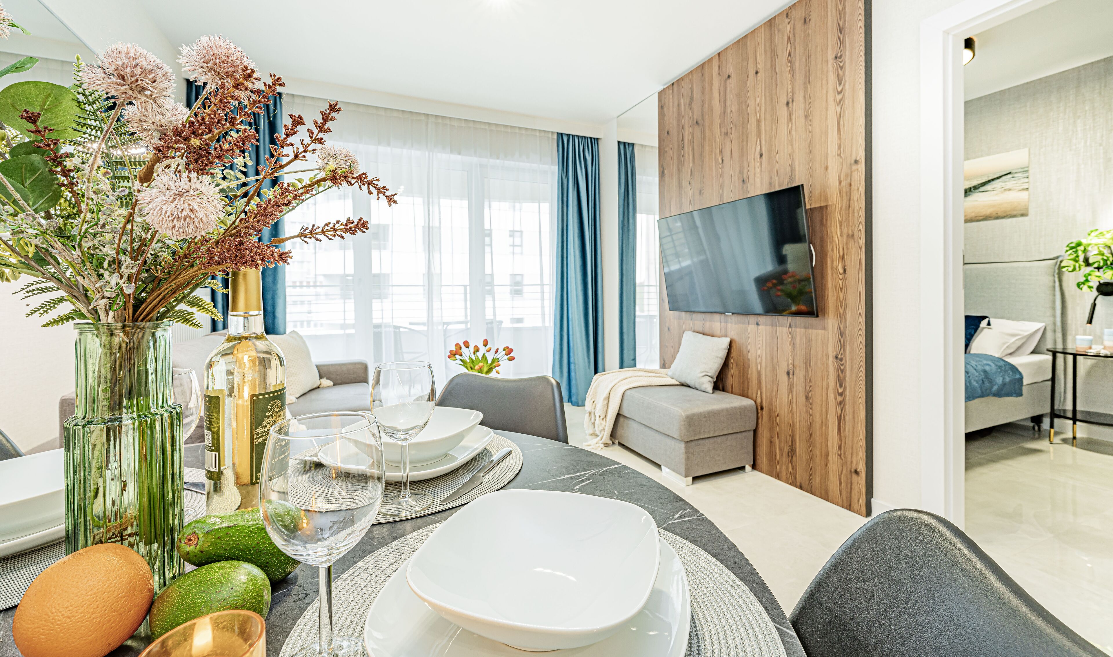 Una sala de estar moderna con comedor, que incluye un televisor grande, asientos cómodos y un jarrón decorativo con flores.