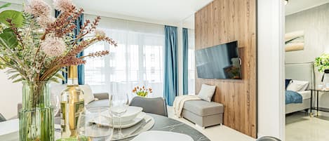 Una sala de estar moderna con comedor, que incluye un televisor grande, asientos cómodos y un jarrón decorativo con flores.