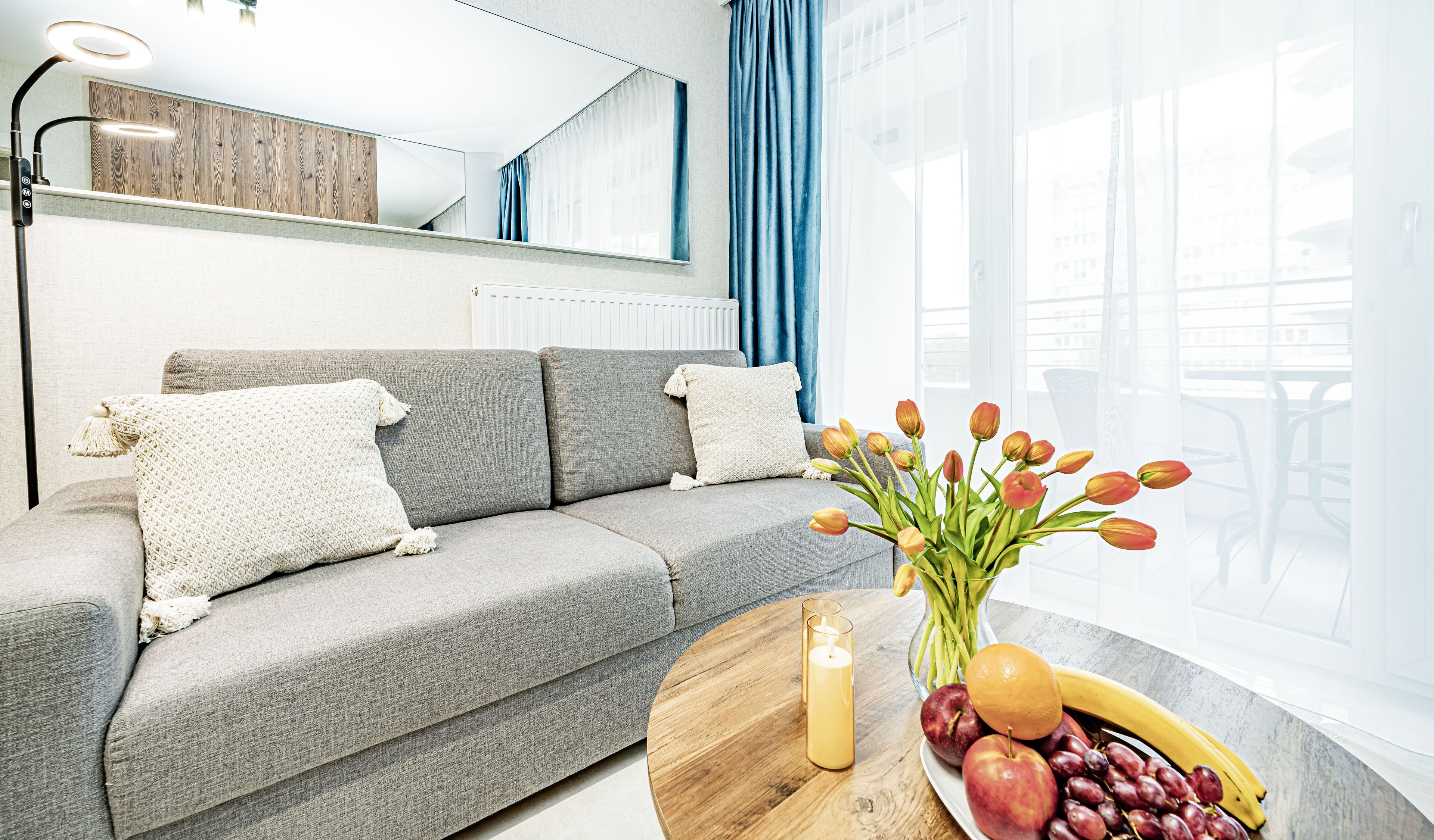 A modern living room with a grey sofa, a round wooden coffee table, and a vase of tulips.