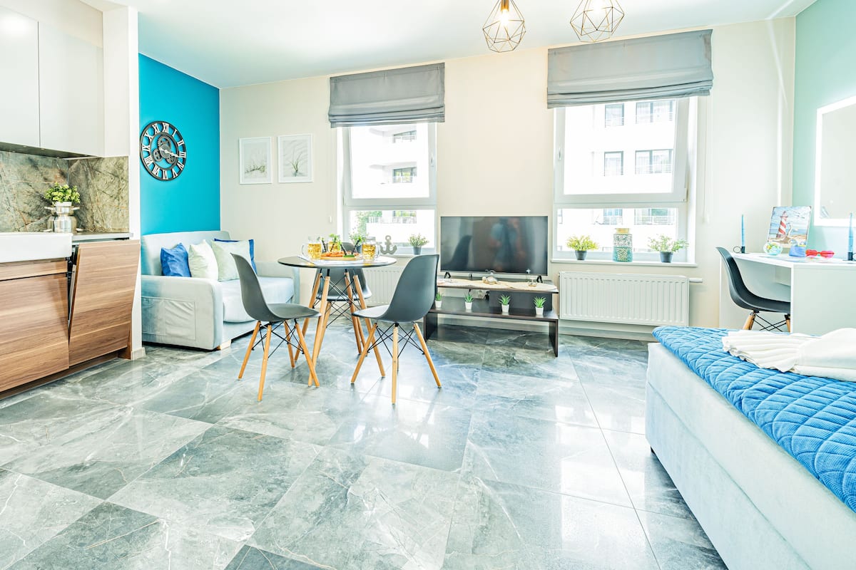 Een modern appartement met een keuken, eethoek en woonkamer. Er is een televisie, een eettafel met stoelen en een bed met een blauwe sprei.