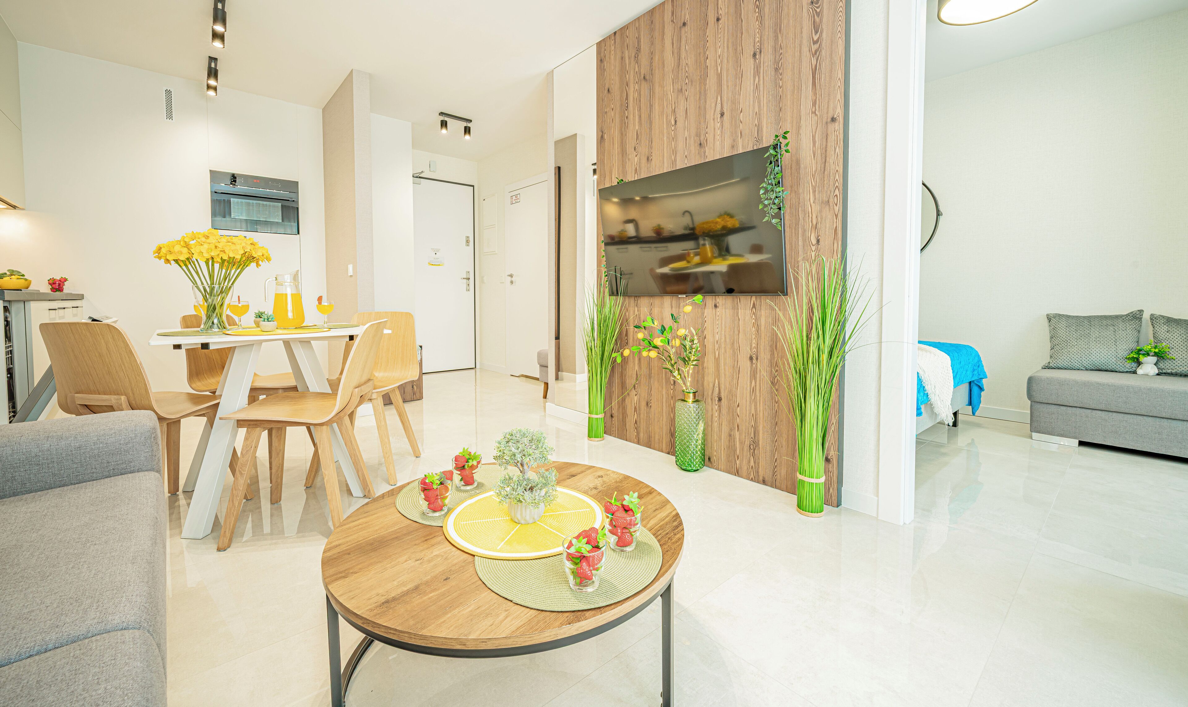 A modern living room with a dining area, a kitchen with a wooden accent wall, and a grey sofa.