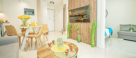 A modern living room with a dining area, a kitchen with a wooden accent wall, and a grey sofa.