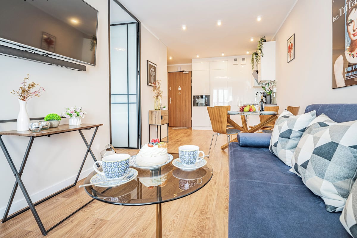 Een moderne woonkamer met een glazen salontafel, een bank en een eethoek met een houten tafel en stoelen.