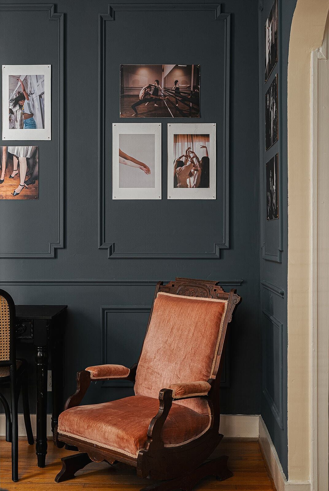 A room with a dark blue wall, a wooden chair with a cushioned seat, and framed photographs.