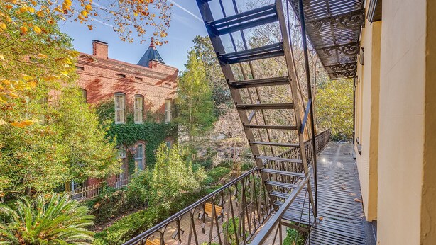 A balcony with a metal railing overlooking a garden and a brick building.