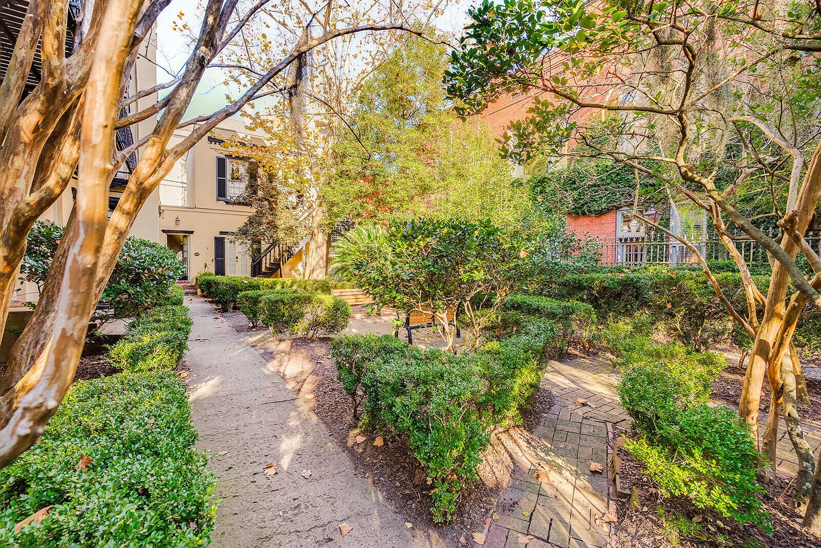 A pathway lined with neatly trimmed bushes and trees, leading to a building with a staircase.