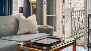 A living room with a sofa, a coffee table, a lamp, and a large window with curtains.