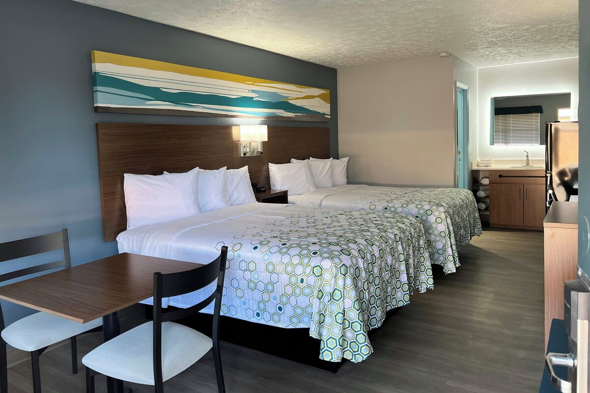 Quarto de hotel com uma cama grande, uma escrivaninha e uma cadeira. Há um quadro na parede e uma janela com persianas.