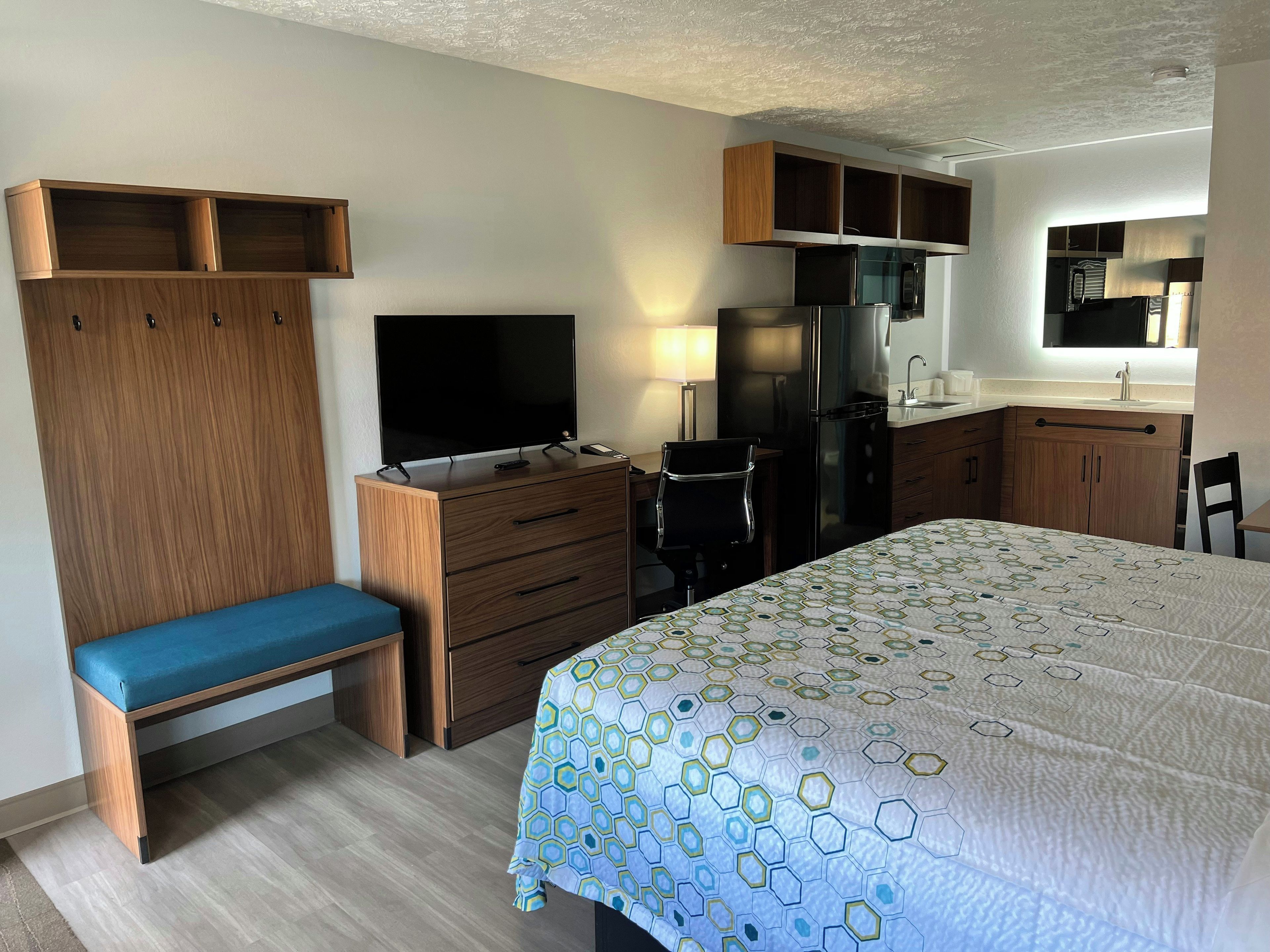 A hotel room with a bed, a desk with a chair, a television, a refrigerator, a microwave, and a small kitchenette.