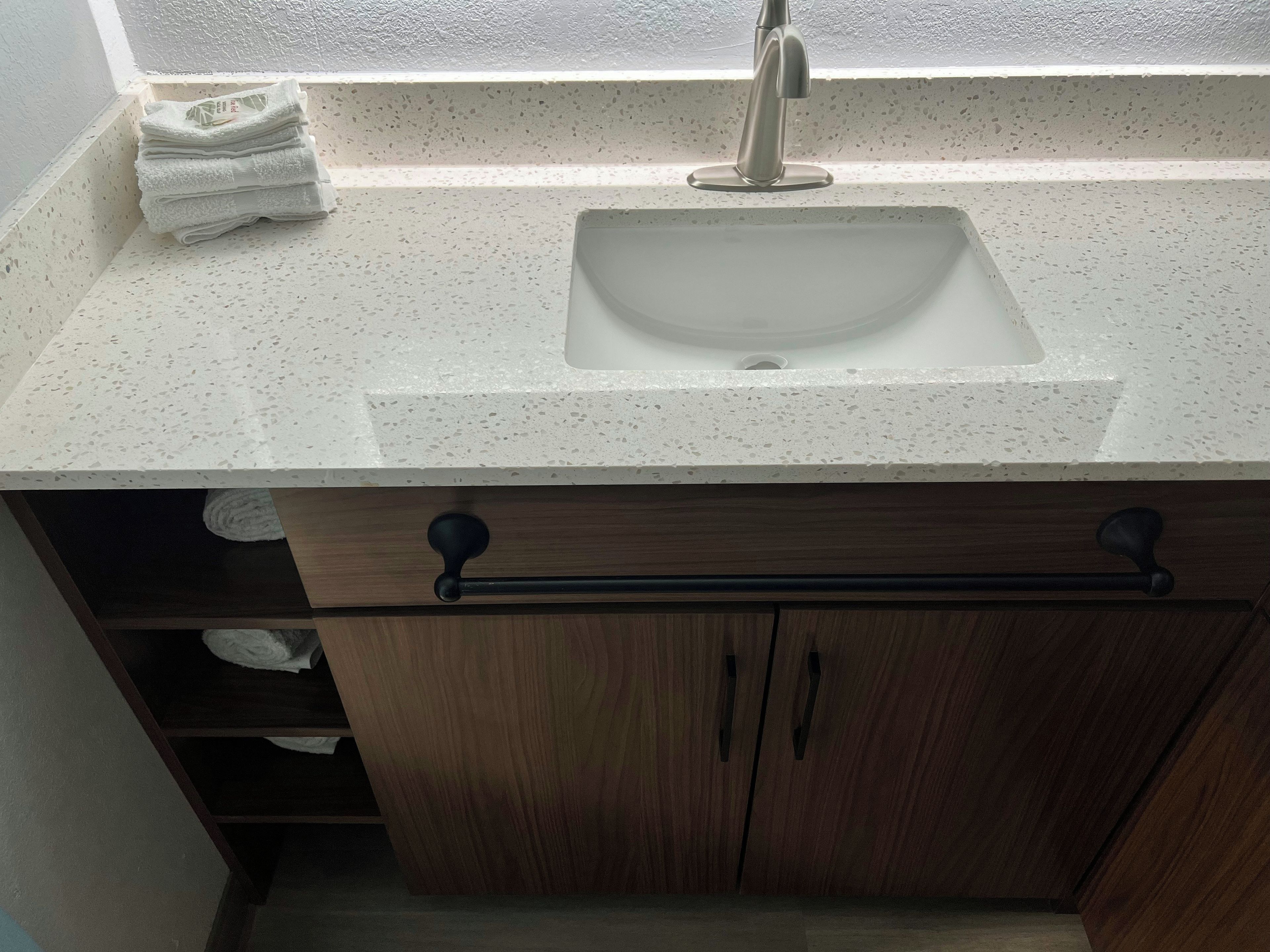 A bathroom with a white speckled countertop, a sink, and wooden cabinets.