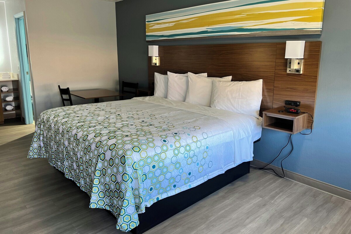Quarto de hotel com uma cama grande, cabeceira de madeira, uma escrivaninha e uma cadeira.