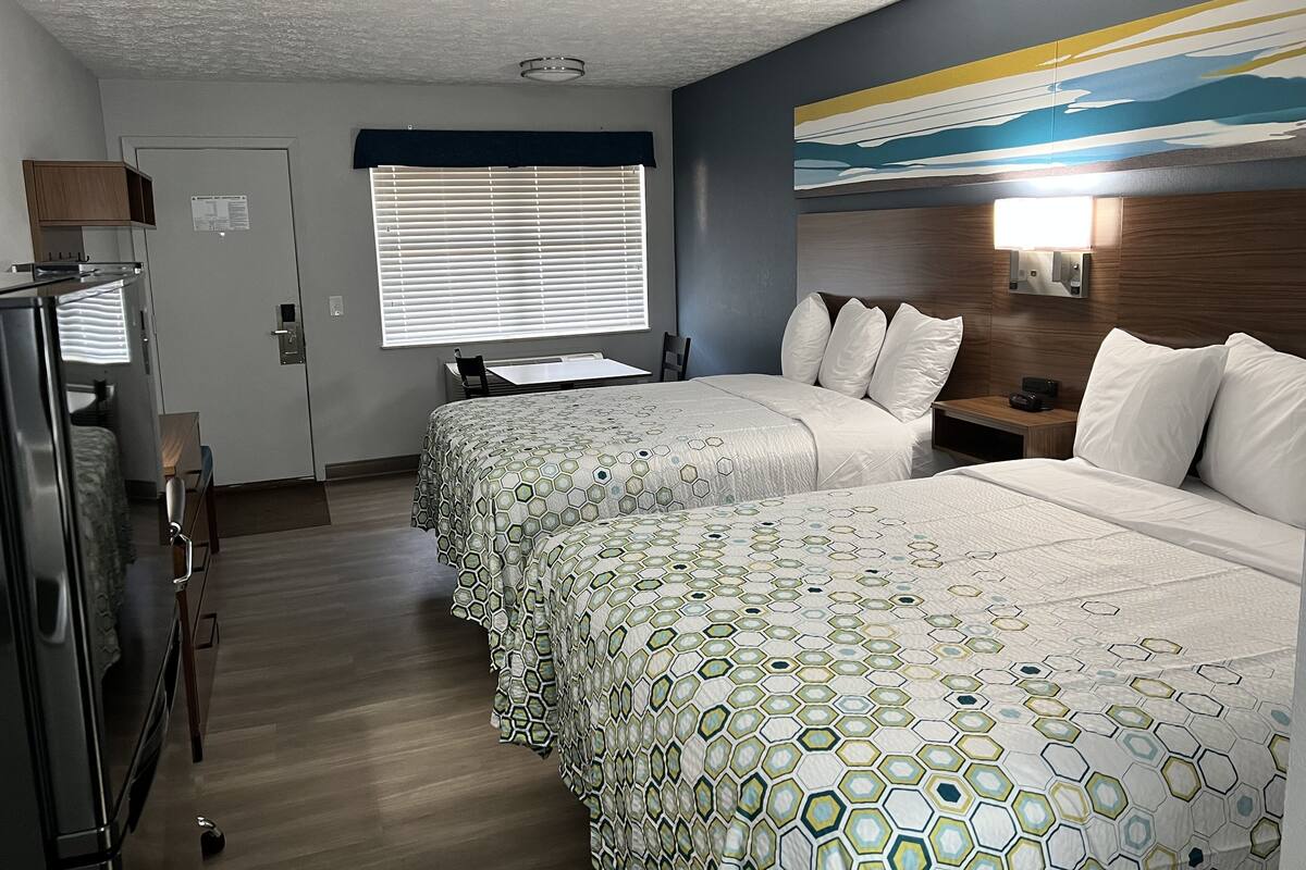 Quarto de hotel com duas camas, uma escrivaninha, um frigorífico e um quadro na parede.