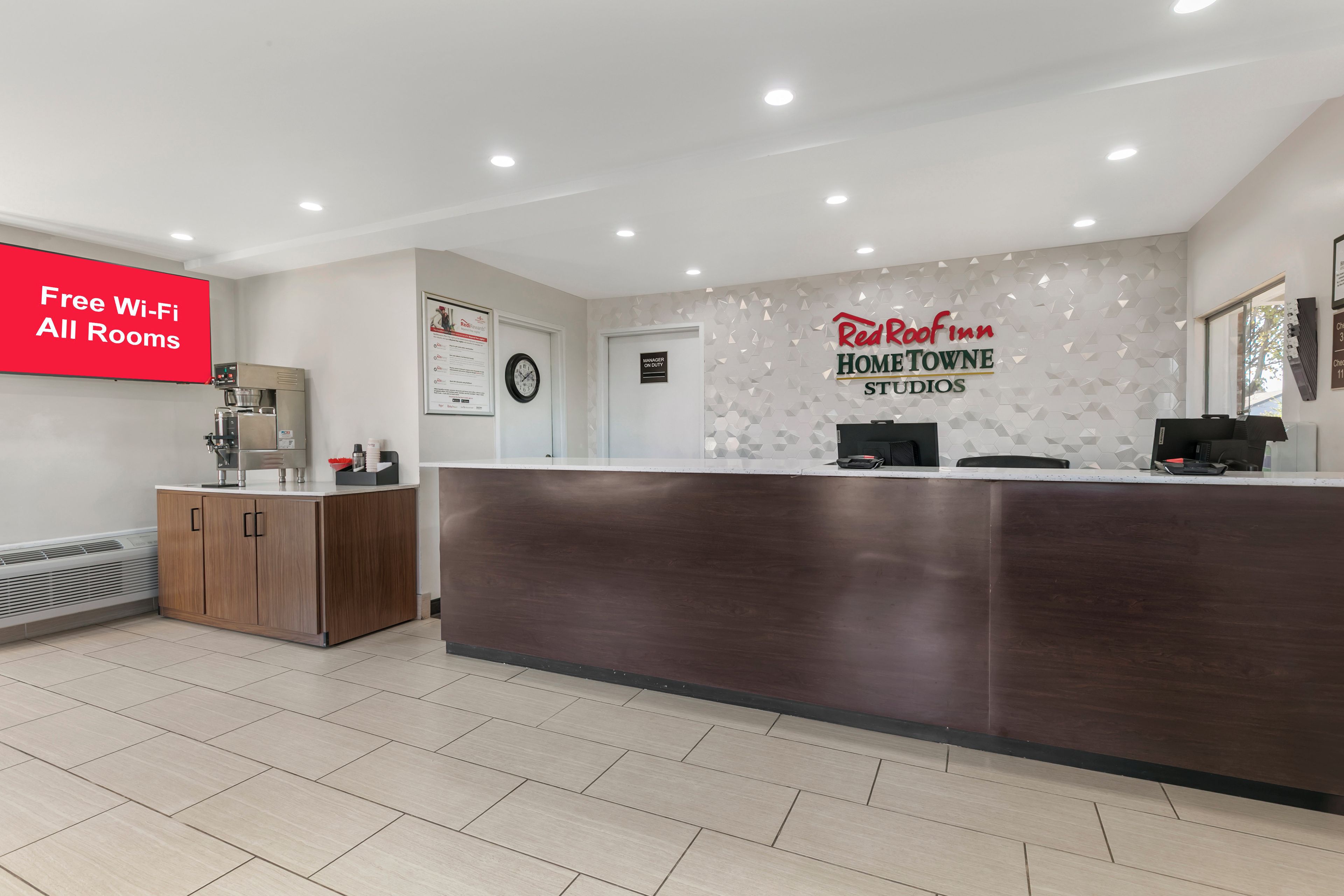 A reception area with a digital screen advertising free Wi-Fi, a clock, and a Red Roof Inn sign.
